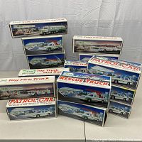 Photo showing multiple Hess toy truck boxes stacked and lined up, including Toy Tanker Truck, Toy Fire Truck, Rescue Truck, and Patrol Car editions with vintage box artwork.