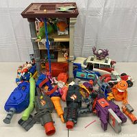 Multiple Ghostbusters items including Firehouse Headquarters playset, proton guns, ghost figures, and Ecto-1 vehicle displayed