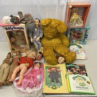 Full lot overview showing large yellow teddy bear, boxed dolls, Mr. Bean doll, loose dolls and Cabbage Patch Kids books and blanket.
