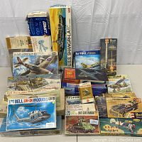 Overview of 15 boxed model kits arranged on table including aircraft, vehicle, ship and car kits