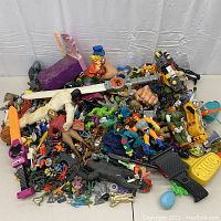 Overview of mixed action figures, weapons and small toys piled on white surface