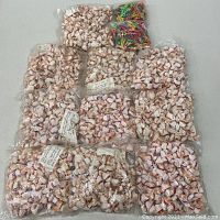 Overview of 10 plastic bags each filled with many small vintage baby dolls tightly wrapped in white cloth with red bands, plus two bags filled with colorful plastic clothespins, all sealed in clear plastic bags.