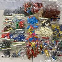 Photo showing numerous plastic toy figures grouped and bagged including soldiers, cowboys, airplanes, animals, and dinosaurs.