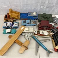 Photo showing assortment of vintage toy vehicles including planes, cars, trucks, boat, and tank on table