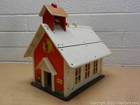 Front and side view of wooden vintage school house with red siding, white roof, front entrance, movable clock, and floral painted base.