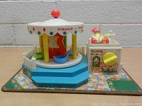 Front and side view of the vintage Fisher-Price Little People Carousel showing the carousel platform with animal figures and the ticket booth with a figurine and crank handle.