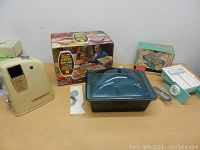 Photo showing beige retro electric heater, blue glass divided food server with lid and box, vegetable slicer with box, and other utensils on table.