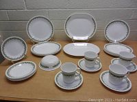 Set of vintage Corelle dishes arranged on table showing plates, cups, saucers, and covered butter dish with green flower pattern.