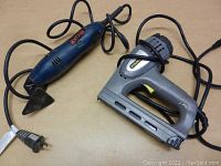 Photo showing Stanley staple/brad gun alongside Ryobi electric sander, both plugged in with power cords visible.