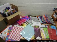 Top view of assorted folded gift bags and multiple tissue paper sheets spread out on a table with some bags packaged inside plastic wrap.