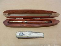 Photo showing the wood pen inside carved wood case next to the vintage pocket knife with carved whale and ship scene.