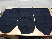 Top-down view showing 12 pairs of black women's underwear neatly laid out on a table in two rows.