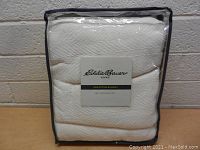 Front view of the white Eddie Bauer Home twin cotton blanket folded and sealed inside clear plastic with black edges.