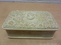 Front view of the cream-colored, intricately carved jewelry box featuring floral patterns and a medallion design on the lid.
