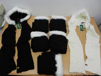 Large lot of six new knit hoodie scarves laid out on a table including five black hooded scarves with white faux fur trim and one white hooded scarf with matching white faux fur trim.