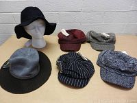 Six women's hats displayed on mannequin head and table, showing various styles and colors, all new with tags.