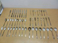 Full set of silver plated flatware laid out on a table showing knives, forks, spoons, and serving spoons arranged in neat rows.