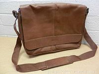 Front view of brown leather flapover crossbody messenger bag showing smooth leather and flap with brand embossing