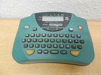 Front view of the teal Brother P-Touch PT-65 label maker showing keyboard and small display screen with some controls.