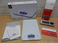 Photo showing Ozeri Touch II digital kitchen scale, user manual, original box, and Rosle digital timer with its box and instruction manual on table.