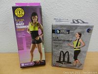 Both boxed items displayed upright: the Gold's Gym plus-size waist trimmer in purple and pink packaging, and the 3 Series Fitness 4 lb weighted vest in gray packaging with a model image.