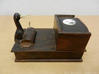 Front and side view showing wooden duck figurine and the rolling mechanism for dispensing cigarettes attached to the base.