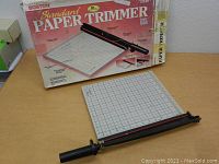 Paper trimmer with cutting arm and box in background, showing full unit.