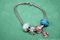Silver tone bracelet with blue, pink, and teal beads and a charm pendant on a green background.