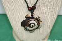 Close-up photo of the turtle pendant showing the detailed spiral design and brown and white coloration.
