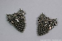 Pair of silver tone figural grape cluster fur clips shown on a neutral background showcasing detailed grape and leaf motif.
