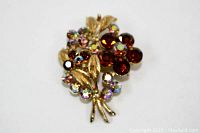 Front view of gold tone metal flower brooch showing reddish-brown center stones surrounded by AB rhinestones and gold textured leaves