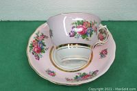 Pink floral teacup with gold trim resting on matching saucer showing design details and condition.