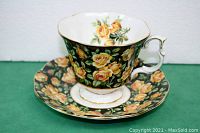 Side view of Royal Albert teacup and matching saucer, showing yellow rose floral pattern on black background and gold trim.