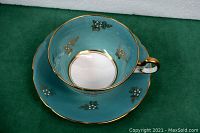 Blue/teal teacup on matching saucer showing floral and gold trim details