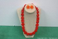 Front view of the orange plastic necklace displayed on a necklace stand alongside a round display for the matching flower earrings.