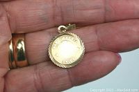 10K yellow gold Aries pendant shown held in hand for scale, engraved with Aries ram symbol, dates and name, with twisted rope border.