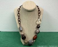 Photo of the brass chain necklace with large various stones displayed on a beige bust stand showing the front view of the necklace.
