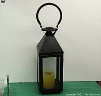 Front view of the black metal hanging lantern with clear glass panels and a faux candle inside, showing the full height and handle for hanging.