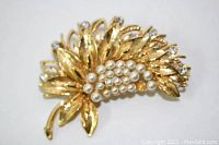 Close-up photo of gold tone brooch showing leaf design with rhinestones and rows of pearls, some pearls visible missing.