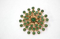 Close-up of vintage gold tone pinwheel brooch with emerald green rhinestones, showing detail of rhinestones and gold tone metal