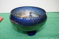 Blue carnival glass bowl with three legs, flower pattern on interior, rippled edge, shown from an angled side view.