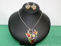 Front view of necklace and matching earrings displayed on black bust showing enamel colors and rhinestone details