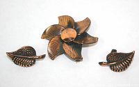 Photo showing copper flower brooch and pair of leaf clip-on earrings on white background.