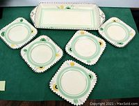 Set of 5 square plates and 1 rectangular serving tray arranged on green fabric