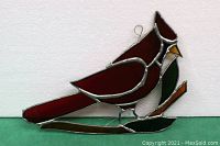 Red cardinal stained glass window hanging shown against a white background, highlighting the detailed glass colors and metal leading of the piece, including the red body, white chest, and green leaves on a brown branch.