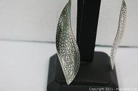 Side view of one earring showing the curved shape and etched floral design in silver.