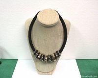 Front view of the full necklace displayed on a beige bust, showing the black bead strands and silver/pearlescent ring elements.