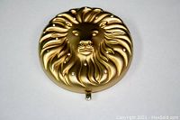 Gold-tone round compact with lion face embossed and rhinestone details on lid.