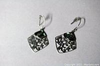 Photo of pair of square sterling silver earrings with cut-out floral design and abalone shell inlay at top corner laid on a white background.