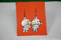 Front view of the pair of cartoon mummy character earrings showing the detailed design with bandages, eyes, and a pink bow on one.